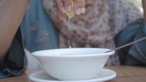 mujer exprimiendo limón en un plato de sopa