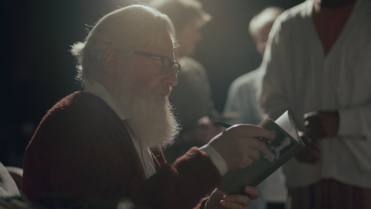 연령의 작가가 무대 위에 앉아서 발매 행사에서 독자에게 책을 서명하고 있습니다.