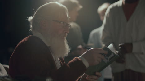 autor anciano sentado en el escenario, firmando un libro para el lector durante el evento de lanzamiento