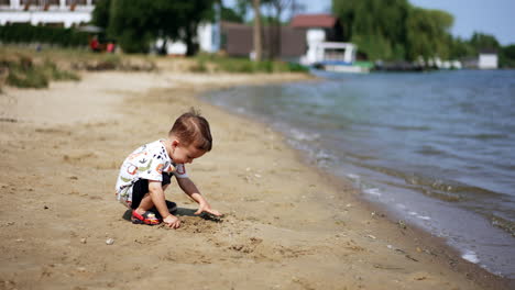 one year old toddler playing in a sand outdoors. happy child on the river bank on sunny summer day.