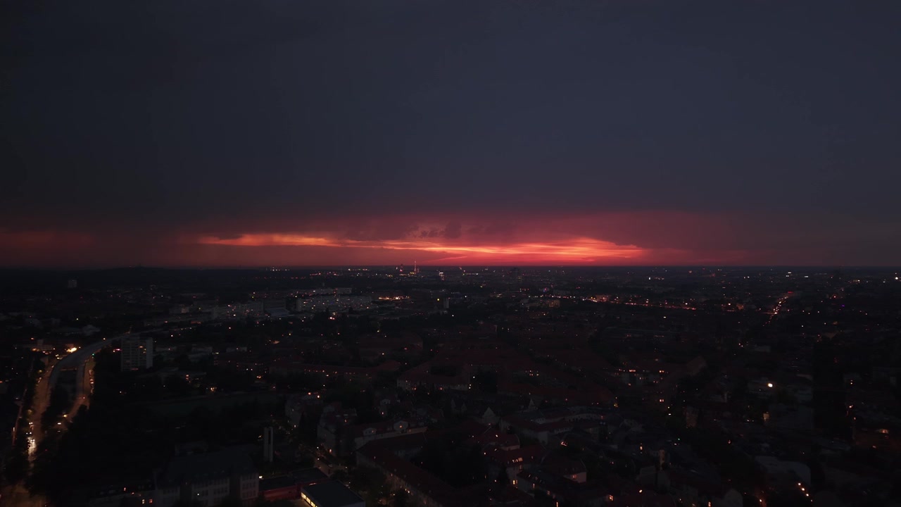 Město s viditelným úderem blesku proti bouřkové obloze, osvětlující městskou krajinu v noci. Krásný letecký pohled, zpětná panoramatická jízda dronem