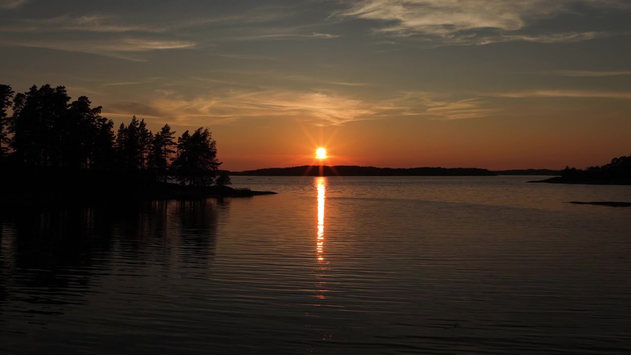 Drone shot gliding over calm lake water with silhouetted pine tree islands