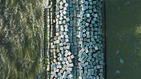 aerial birdseye view of protective stone pier with concrete blocks and rocks at baltic sea coastline at liepaja, latvia, strengthening beach against coastal erosion, drone shot moving forward