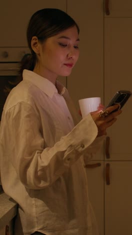 woman using phone and drinking coffee in kitchen