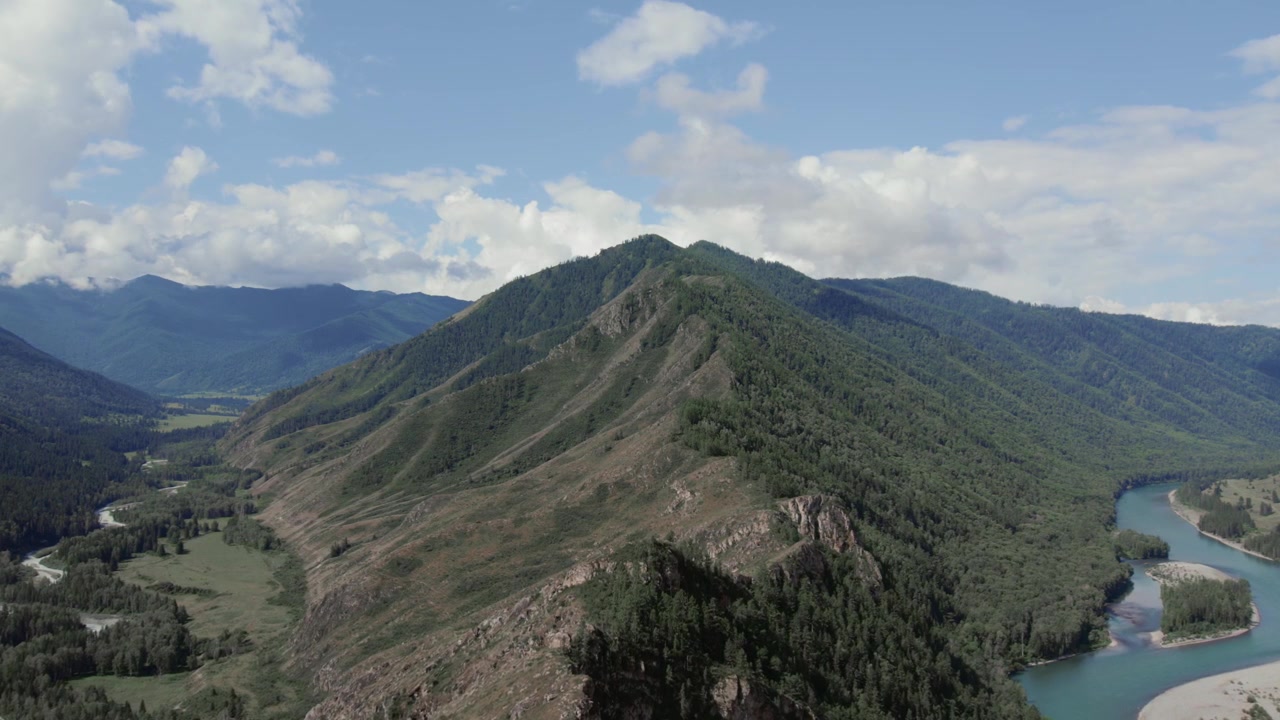 Metraje de dron del valle de Ak-Kem en las montañas de Altai, Rusia, con un río turquesa serpenteante, crestas boscosas y nubes imponentes sobre un paisaje remoto y salvaje