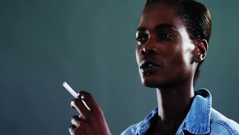 androgynous man posing with cigarette against dark background
