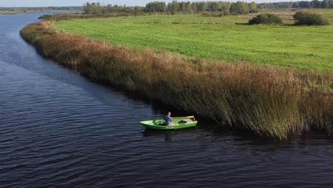 circulating drone shot with man on fishing boat who are fishing in the river near reeds