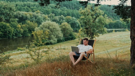calm relaxed man sits in a folding chair in nature. businessman uses laptop working remotely.