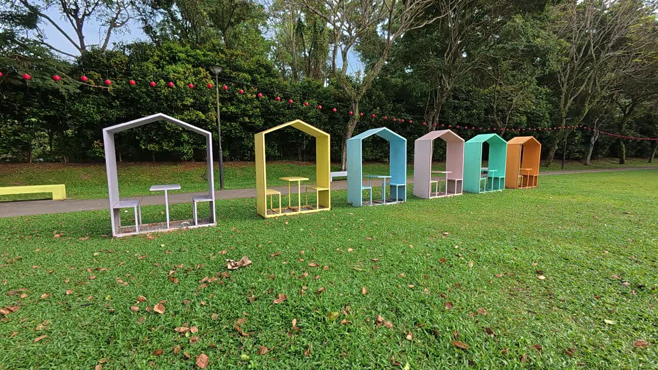 This video showcases colorful, covered benches in a Malaysian public park, neatly arranged in a row. Each bench accommodates two people, providing a shaded and inviting spot for relaxation.