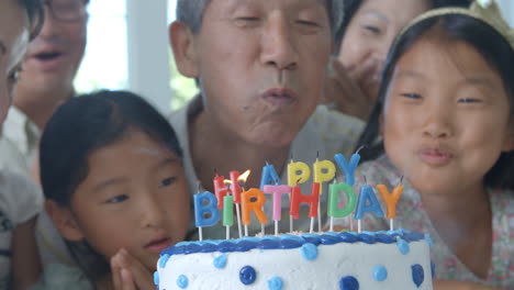 grandfather blows out candles on birthday cake