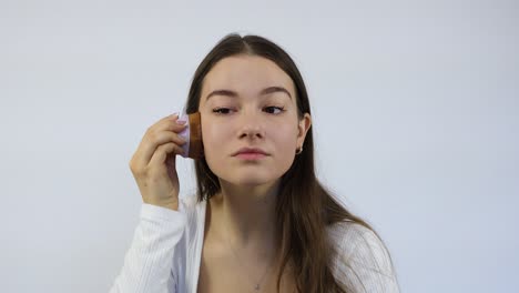 Attractive-young-woman-sitting-alone-in-front-of-the-mirror-and-applying-makeup-with-the-brush-in-front-of-the-white-background