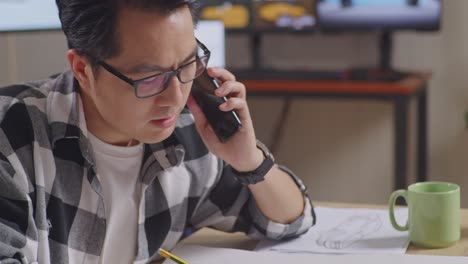 close up of asian male talking on smartphone while working on a car design sketch on table in the studio