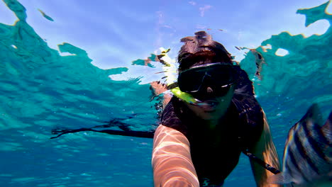 un niño buceando y nadando en la superficie del agua filmando un video selfie con máscara y tubo de snorkel | turista filmando su experiencia de snorkel