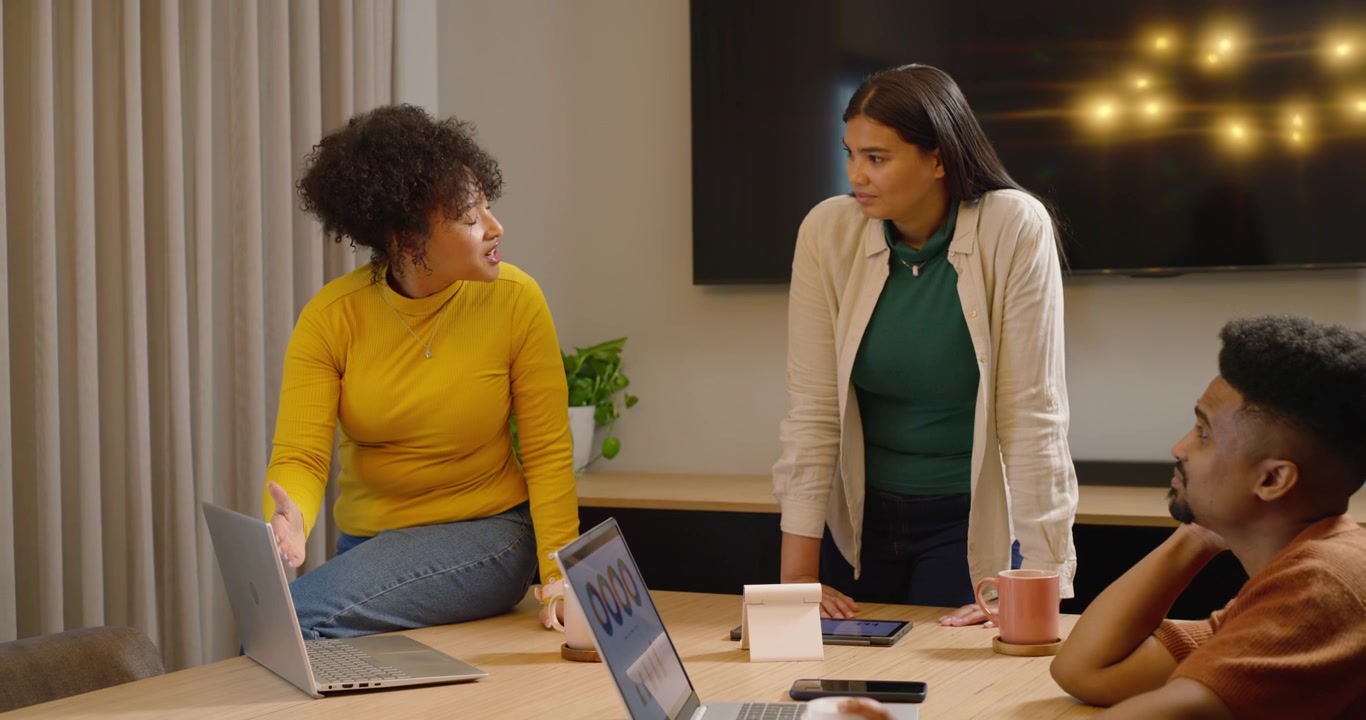 African American team watching woman in yellow top opening point, explaining laptop charts at table