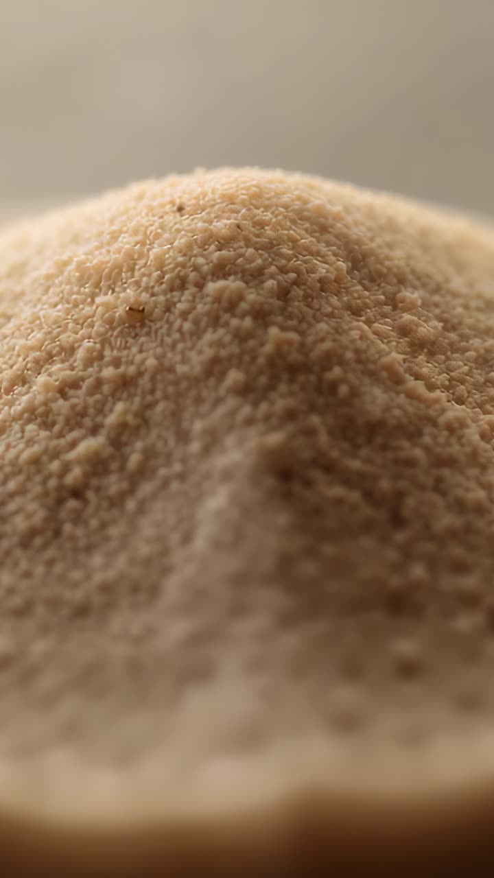 Vertical video: Adjusting camera bringing beige powder into sharp focus on dish showing left speck