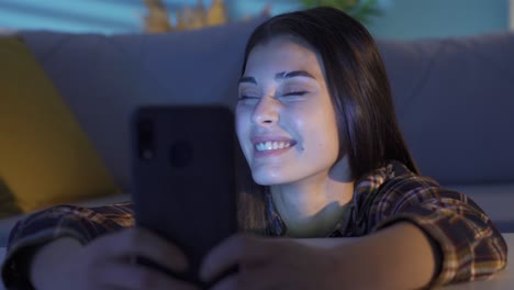 chica joven sentada en casa usando el teléfono y sonriendo.