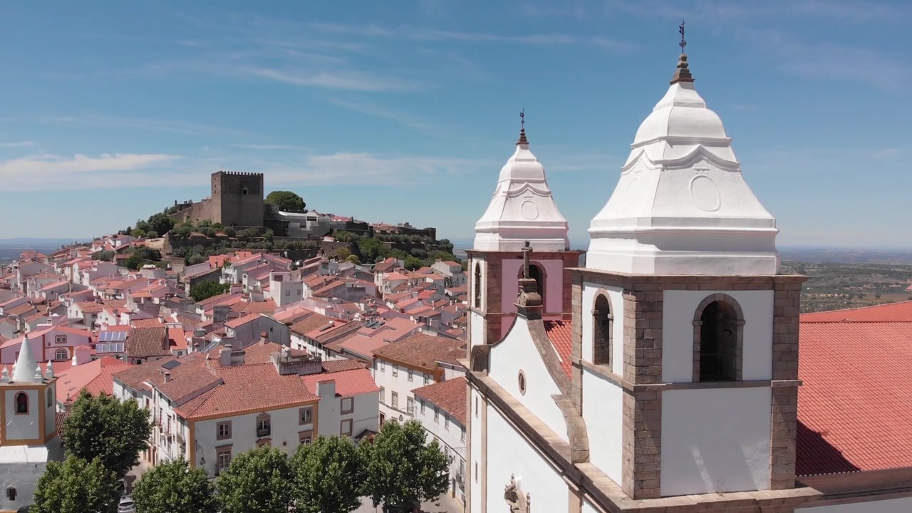 Ripresa aerea con drone in discesa davanti alla facciata della chiesa, con il castello sullo sfondo