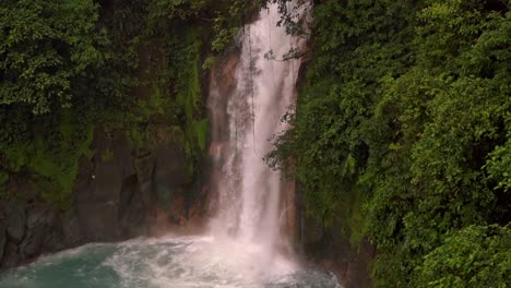 the dense, green rainforest foliage surrounds the scene, highlighting the mystical and ethereal atmosphere of the rio celeste waterfall in costa rica