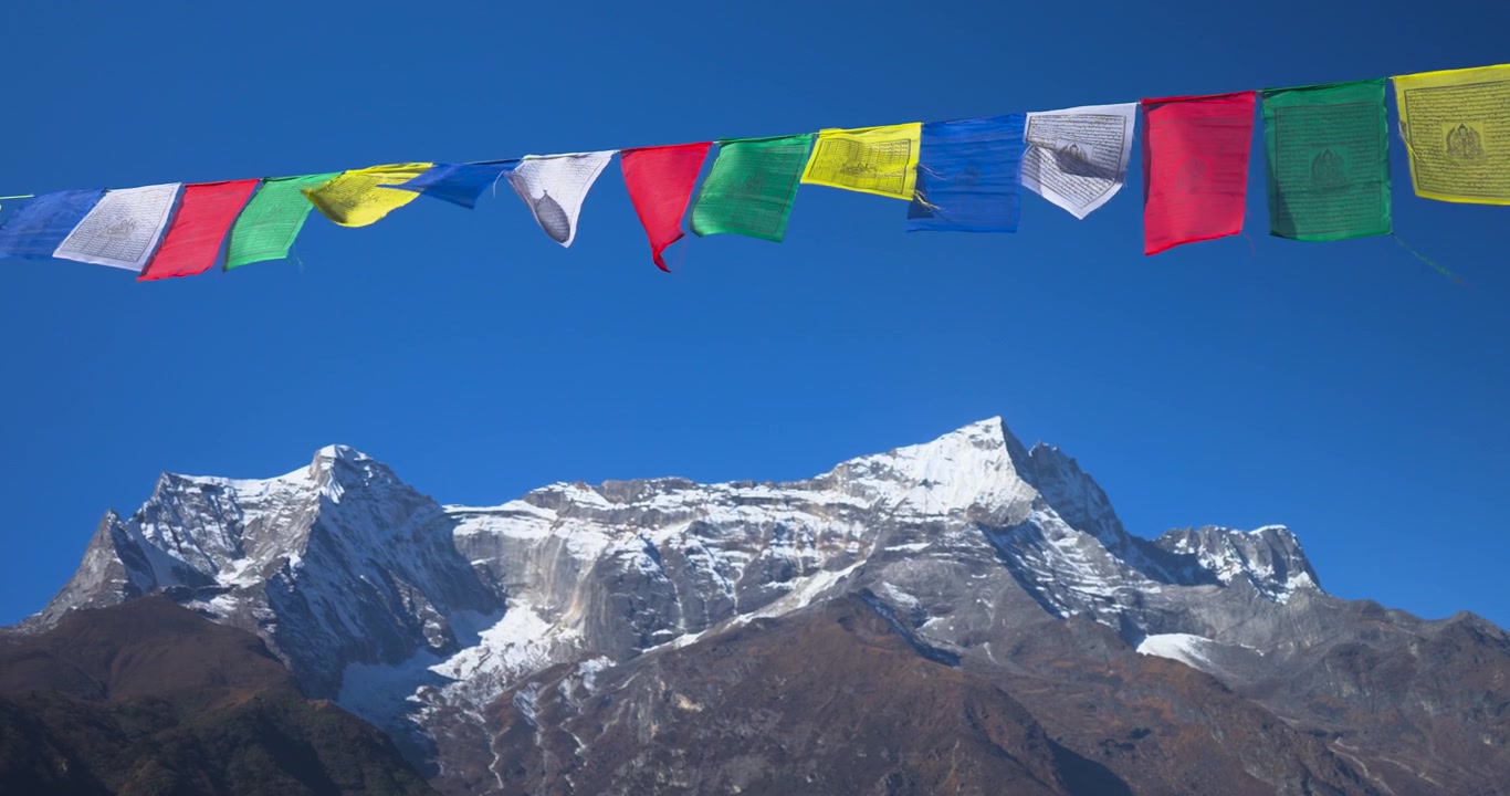 Everest region, Nepal, static shot of the snow capped Kongde Ri mountain range framed below a string of colorful Buddhist prayer flags