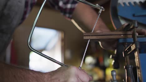 Cerca-De-Las-Manos-Del-Fabricante-De-Cuchillos-Masculino-Caucásico-En-El-Taller-Usando-Una-Sierra