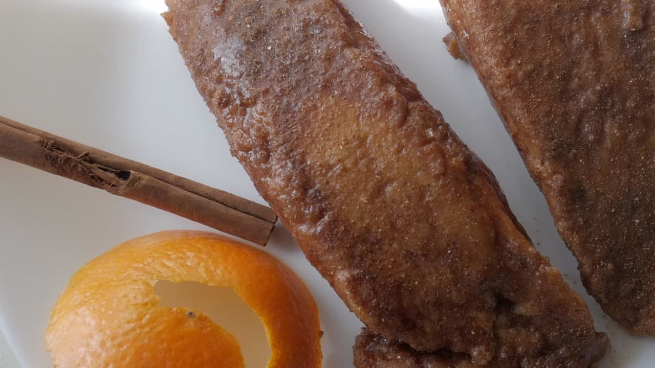 Delicious Torrijas with orange peel and cinnamon stick served on a white plate