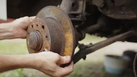 Rusty-disc-brake-car-part-being-removed-from-car-axle-by-technician