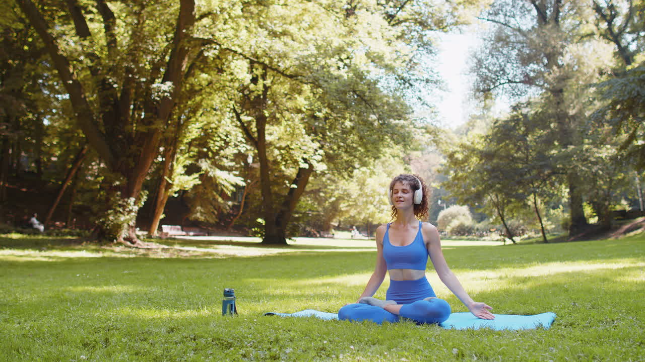 mujer sentada en una alfombra en posición de loto relajándose practicando meditación de yoga en el parque en un día de verano