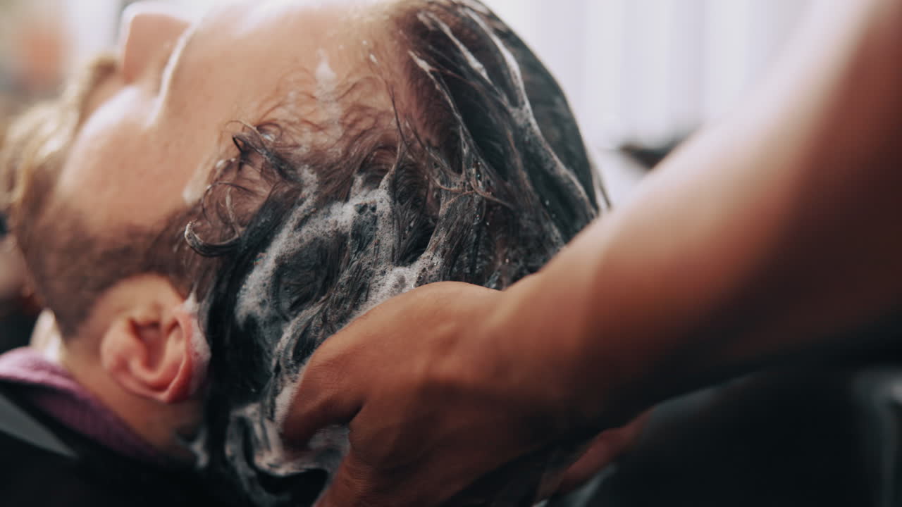 Primo piano di un uomo a cui vengono lavati e massaggiati i capelli in salone