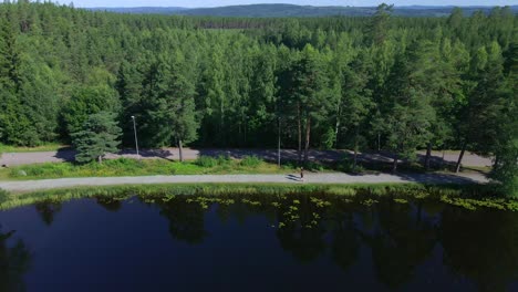 reversing drone footage over a small lake showing two runners on a gravel path with forest behind them