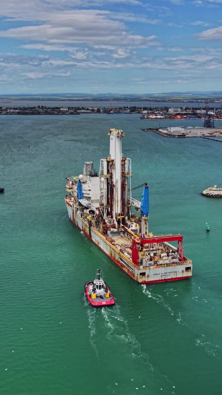 Large ship moves through calm water towards port in clear weather