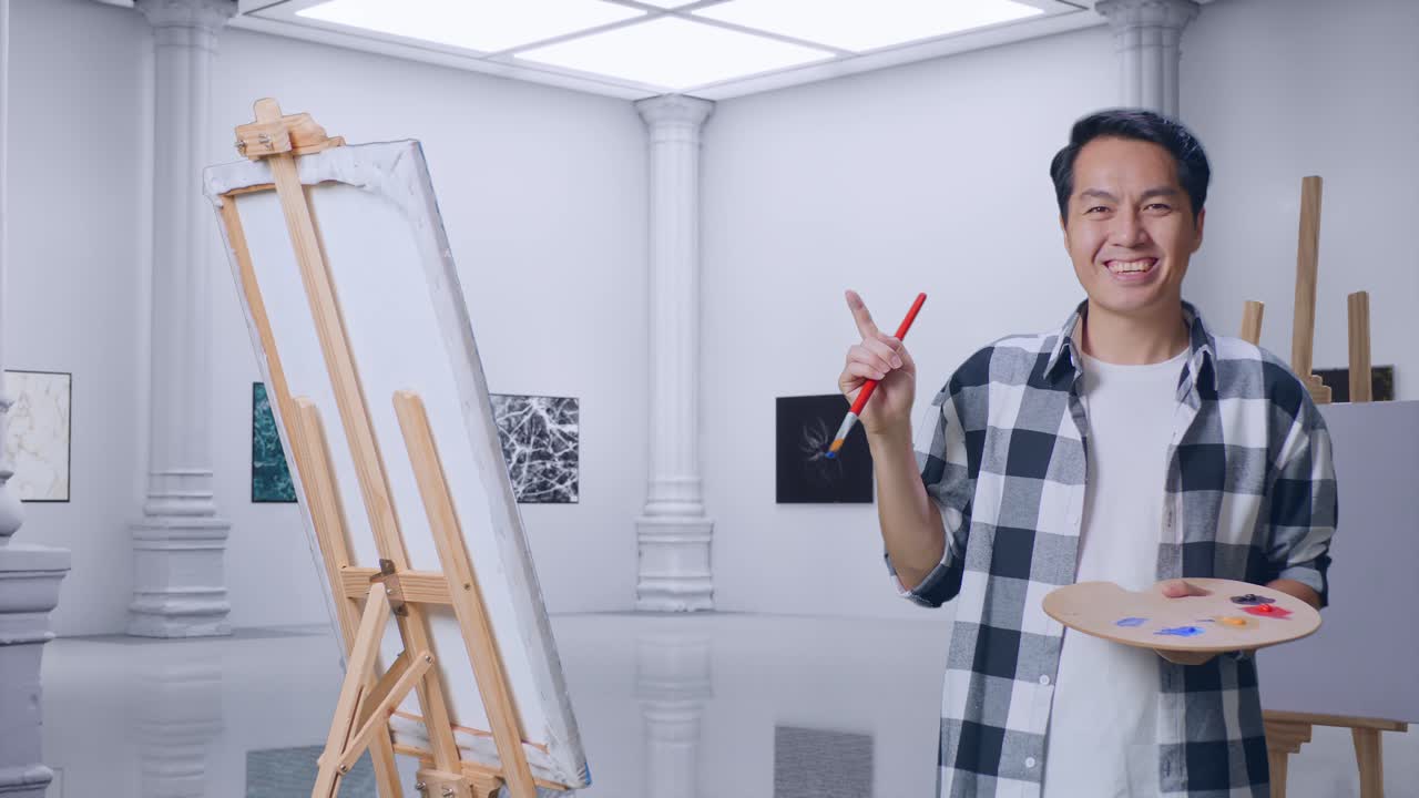 아시아 남성 예술가 가 갤러리에서 오일 페인트와 브러쉬로 그림을 그리면서 캔버스를 가리키고 있다