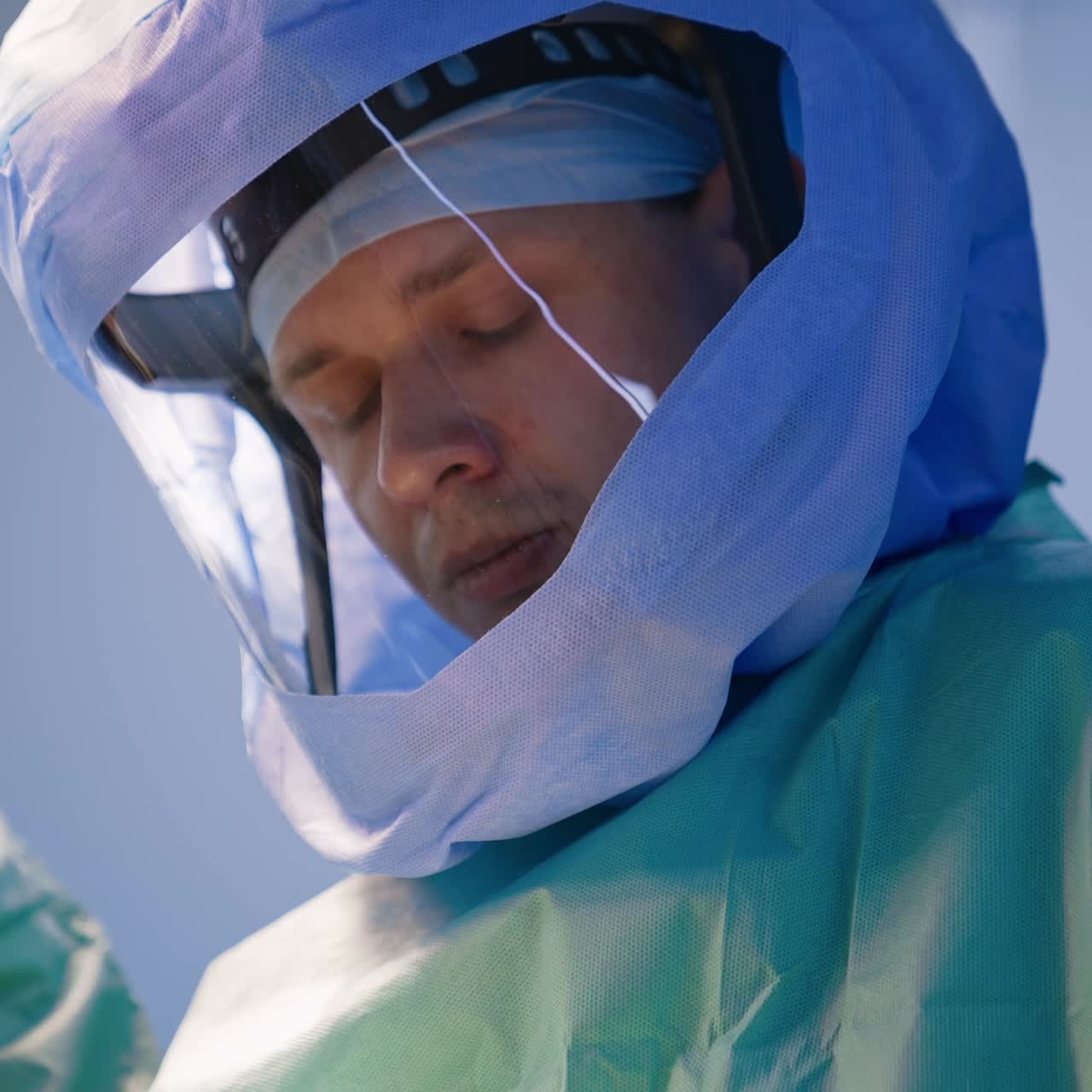 Mid-aged Caucasian surgeon in protective helmet looks down at the operated area. Portrait of a confident doctor at work