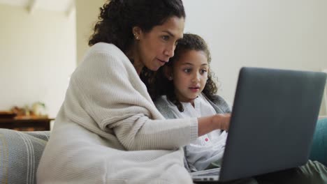 Happy-mixed-race-mother-and-daughter-sitting-on-the-sofa,having-fun-and-using-laptop