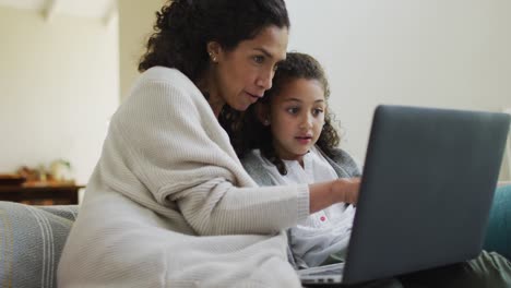 Feliz-Madre-E-Hija-De-Raza-Mixta-Sentadas-En-El-Sofá,-Divirtiéndose-Y-Usando-Una-Computadora-Portátil