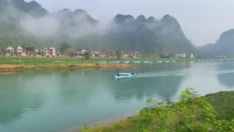 un barco que lleva a un turista a un largo y hermoso río esmeralda con la montaña nublada en el fondo