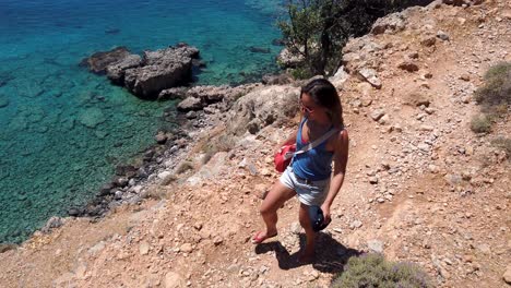 woman with loose hair filmed from above walks on the edge of a cliff and admires the transparent sea below