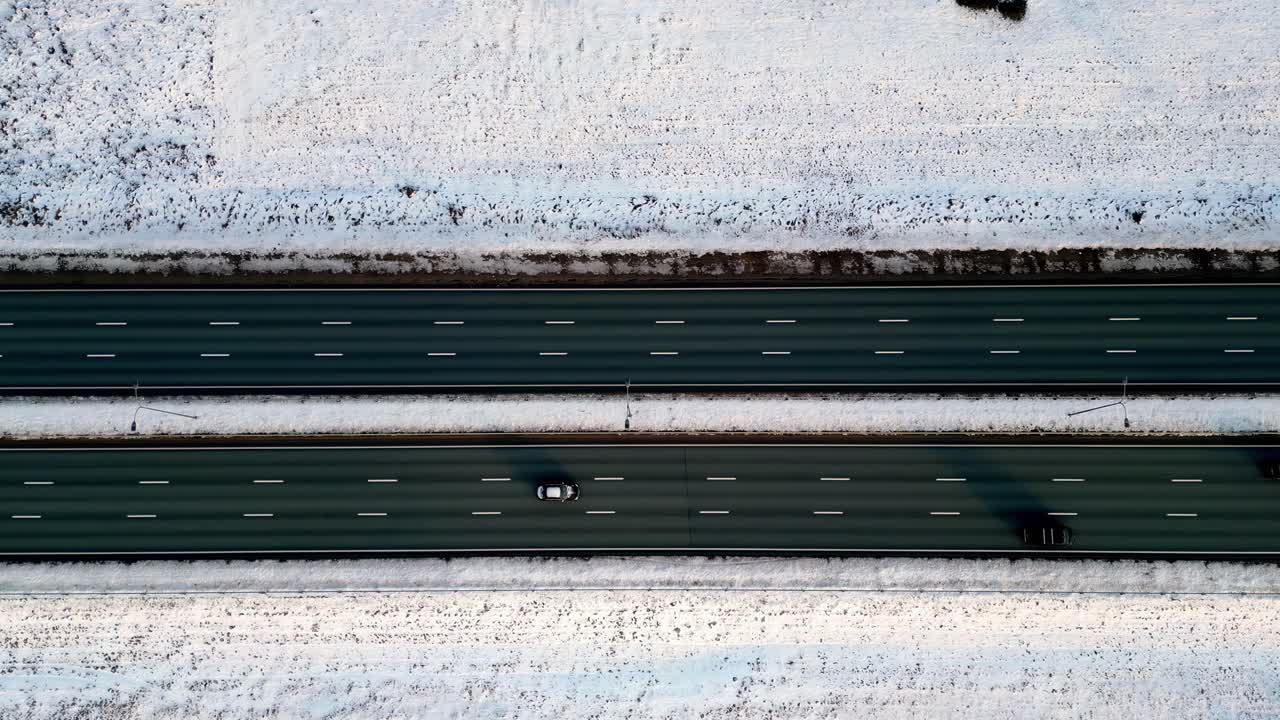 다중 차선 고속도로의 풍경적인 공중 풍경, 부분적으로 고 눈으로 인 상록 나무로 여 있으며, 겨울의 경이로운 땅에서 몇 대의 자동차가 도로를 따라 이동합니다.