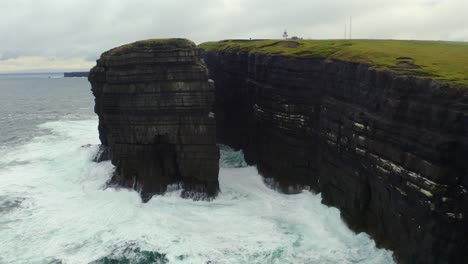 spectacular drone orbit of loop head peninsula, revealing the gap between sea stack and cliffs with lighthouse