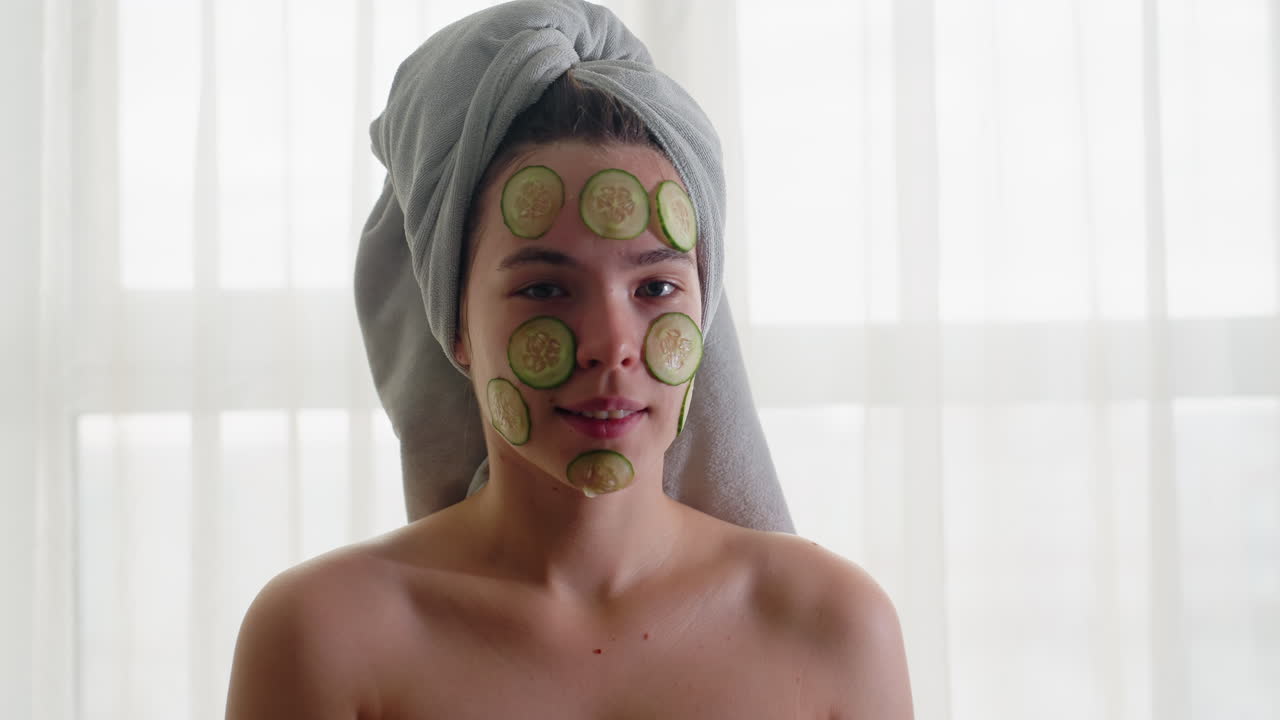 Portrait view of woman relaxing with cucumber slices on her face, wrapped in towel, she enjoys spa treatment at home, with fresh, natural ingredients for skin care and rejuvenation
