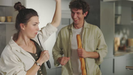 playful couple singing and dancing in kitchen with cooking utensils