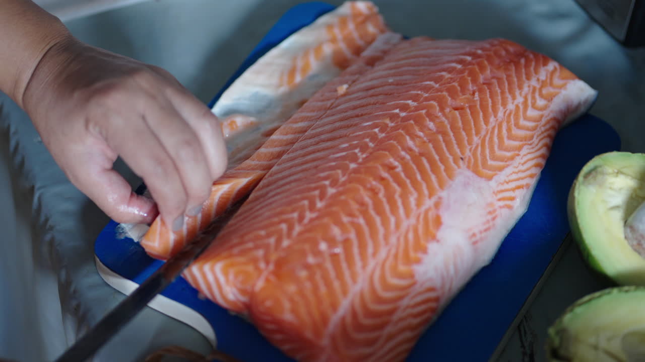 White hands cutting salmon slices for sushi in close-up from above in kitchen scene