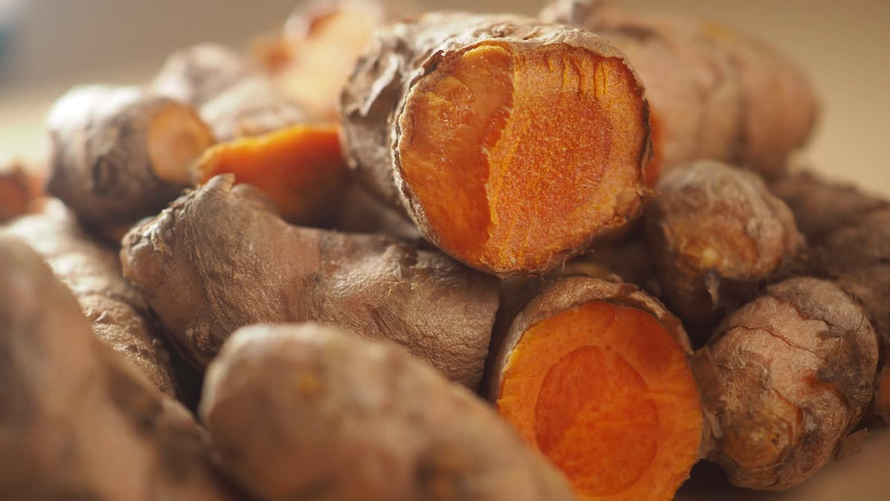 Primo piano di radici fresche di curcuma, alcune tagliate per rivelare l'interno arancione