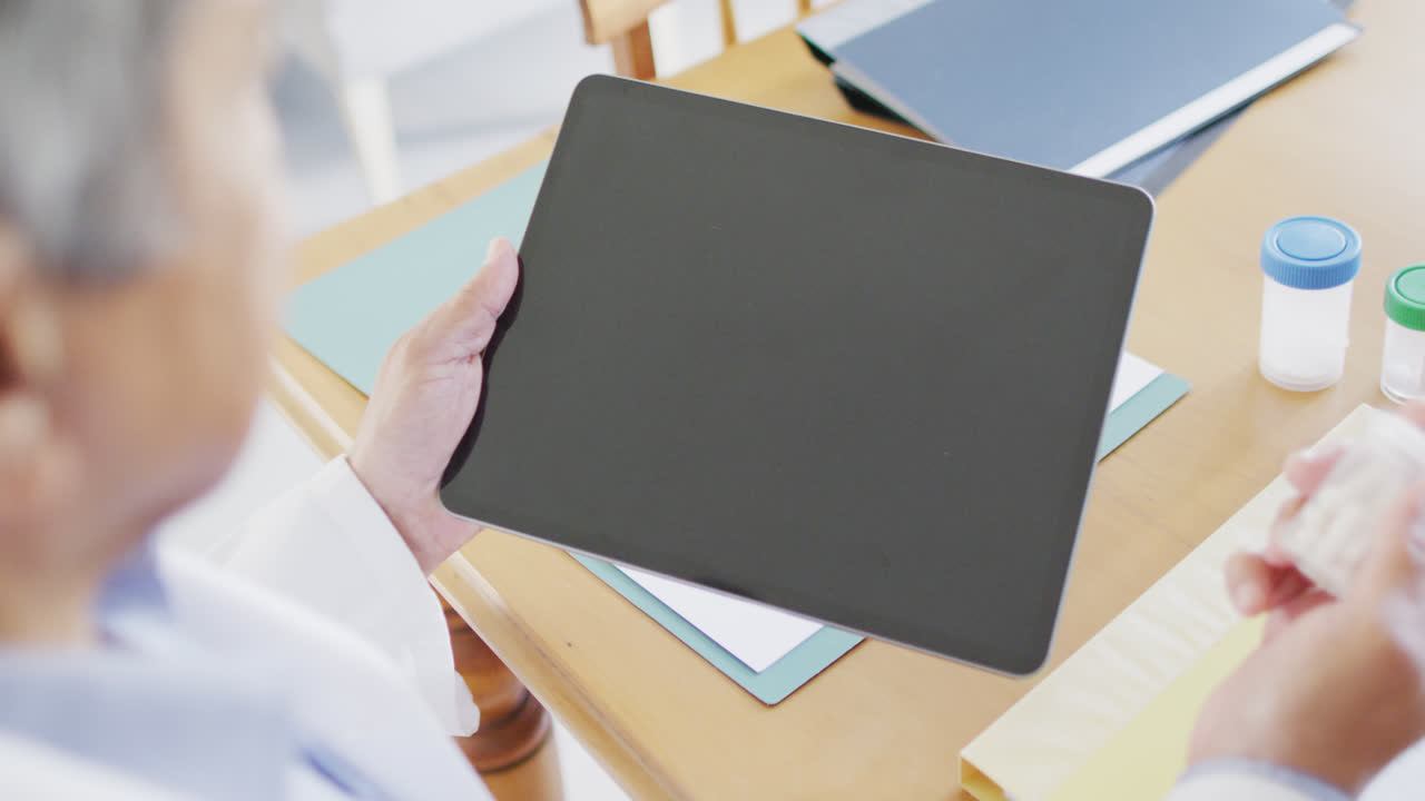 태블릿을 사용하고 약을 들고 있는 수석 남성 의사, 화면에 있는 공간을 복사합니다.