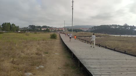 people strolling over a wooden boardwalk near the beach on a cloudy gray morning, take a panoramic view. porto-novo, galicia, spain