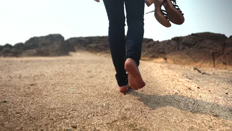 chica flaca india caminando en la playa en paños negros sin sandel en la mano