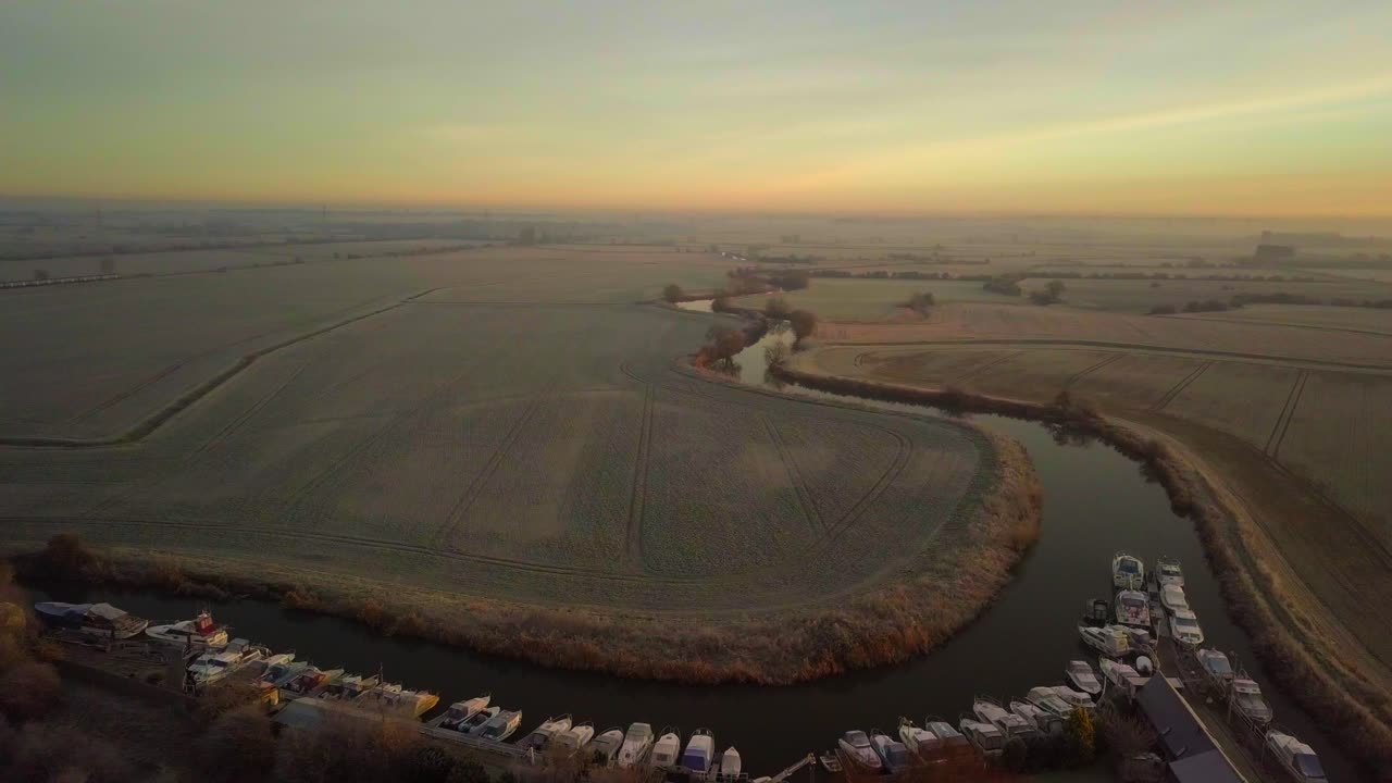 드론은 얼어붙은 과 은 강 위를 날아다니며 태양이 오른쪽으로 뜨고 있습니다.