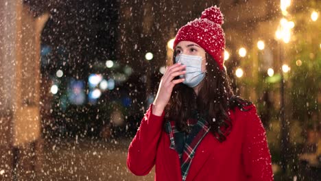 Nahaufnahme-Einer-Kaukasischen-Frau-Mit-Medizinischer-Maske,-Die-Auf-Der-Straße-Hustet,-Während-Es-Zu-Weihnachten-Schneit