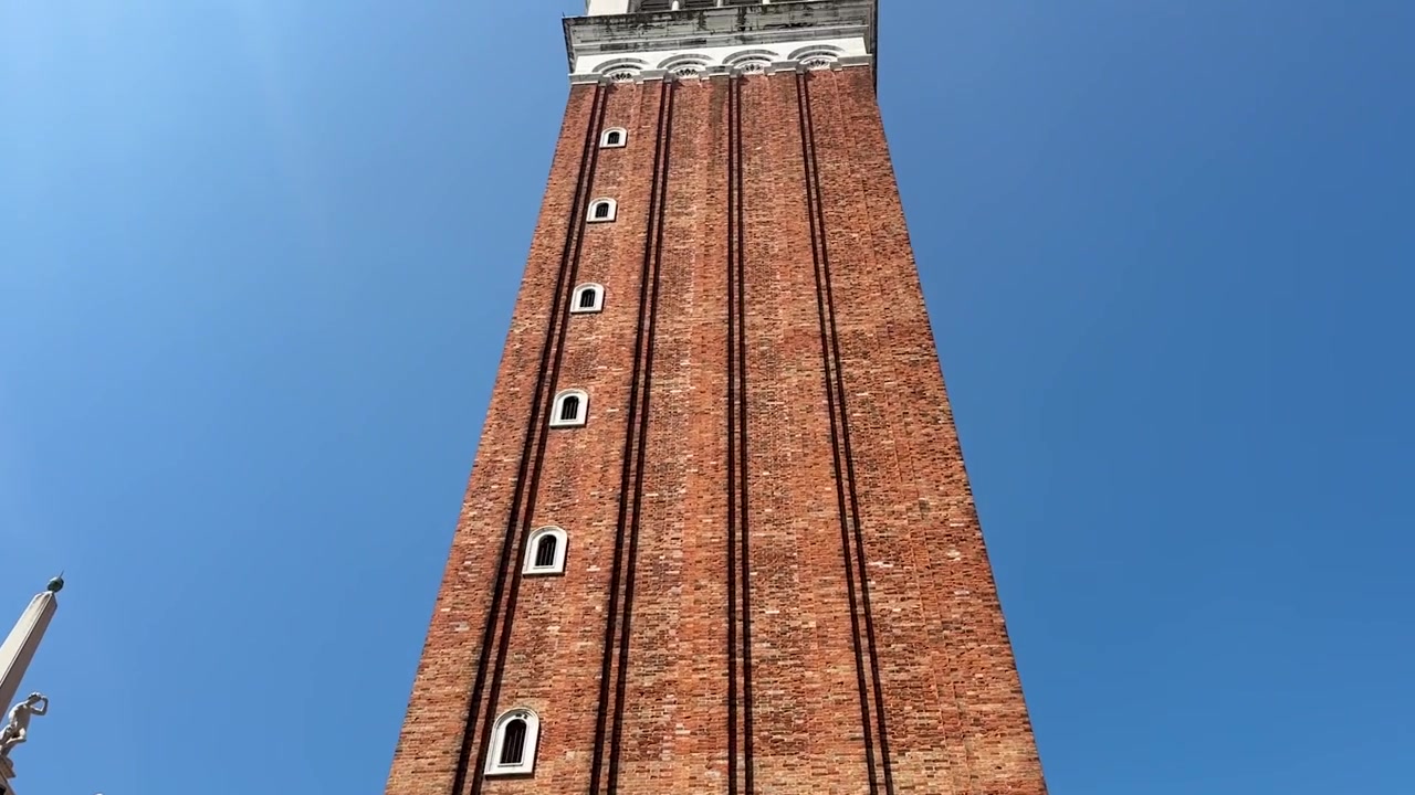 Filmato cinematografico che effettua una lenta panoramica verso l'alto per rivelare drammaticamente l'iconico Campanile di San Marco che svetta su Piazza San Marco, uno dei punti di riferimento più riconoscibili e mozzafiato di Venezia, Italia.