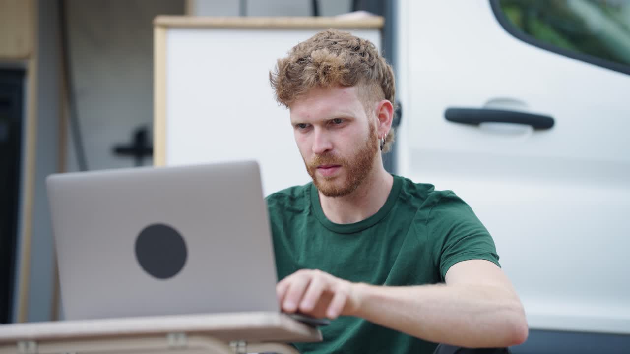 Man working on laptop in front of van