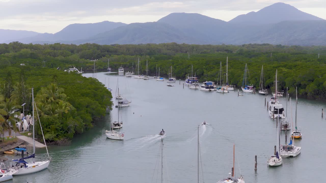 Aerial footage captures boats and lush greenery at Port Douglas marina. Calm waters and overcast skies create a serene atmosphere